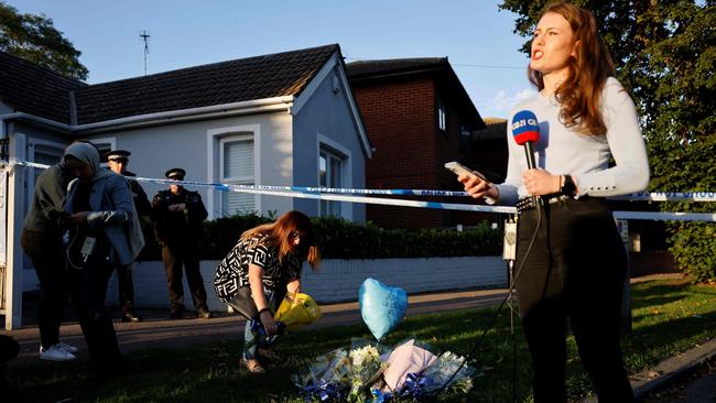 A wellwisher places a floral tribute as a journalist speaks to camera at the scene. Picture: AFP