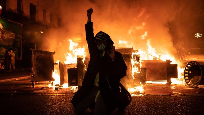 A BLM demonstrator raises a fist as a fire burns in the street after clashes with law enforcement near the Seattle Police Department’s East Precinct.