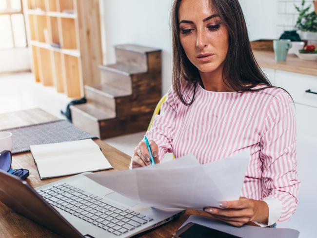 Woman working with documents and computer in the kitchen at home. Source: iStock.