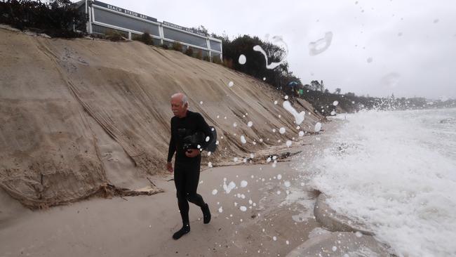 Byron Bay resident Reed Waters walks past the Beach Cafe as the surf pounds the NSW beach. Picture: Jason O'Brien