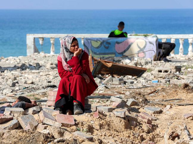 A woman sits by rubble as she waits along Gaza's coastal al-Rashid Street for people to cross from the Israeli-blocked Netzarim corridor from the southern Gaza Strip into Gaza City on January 26, 2025. Israel said on January 25 it would block the return of displaced Palestinians to their homes in northern Gaza until Arbel Yehud, one of the hostages taken captive during the October 7, 2023 attacks, is released. Hamas sources said that Yehud was "alive and in good health", and would be "released as part of the third swap set for next Saturday", on February 1. (Photo by Omar AL-QATTAA / AFP)