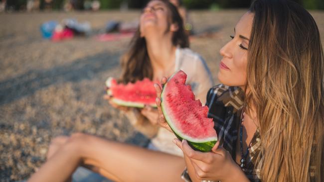 Gold Coast Bulletin — Good Health Guide — Spring cleaning. Girlfriends laughing and eating watermelon on the beach. Sunset