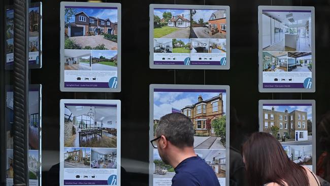 Pedestrians look at residential properties displayed for sale in the window of an estate agents.