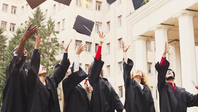 A group of multietnic students celebrating their graduation by throwing caps in the air. Education, qualification and gown concept.