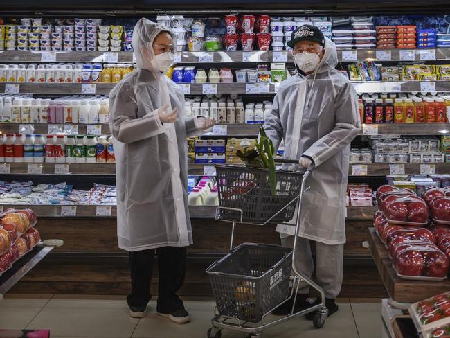 A Chinese couple wear plastic coats and protective masks as they shop for groceries at a supermarket in Beijing, China. Picture: Getty Images