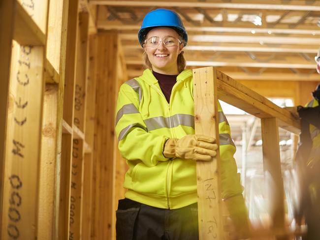 a female construction worker carries some studwork on a building site housing development and is assited by a male colleague .