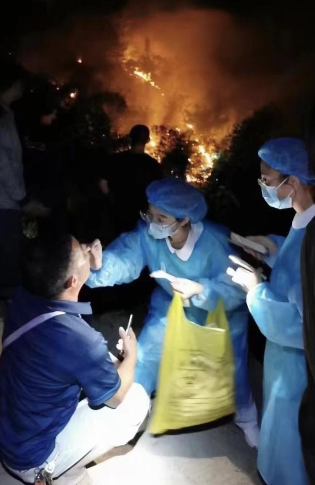 Two Chinese healthcare workers perform a mandatory Covid test just metres away from a wildfire in Chongqing. Picture: Twitter/StephenMcDonell