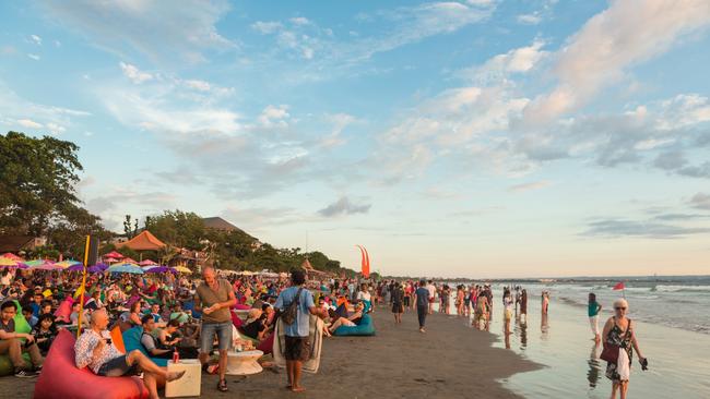 A large crowd of tourists, Indonesian and foreigners, enjoy the sunset at a beach bar on Kuta beach in Seminyak, Bali.