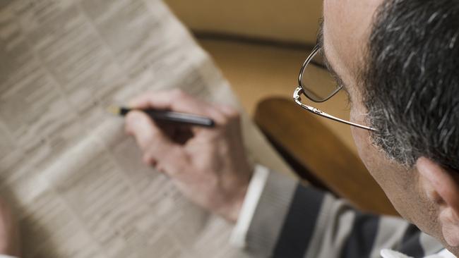 A man looks for job opportunities in a newspaper.