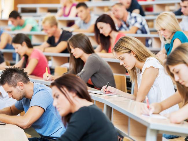 "Group of college students in the university amphitheatre, they are sitting and doing an exam."