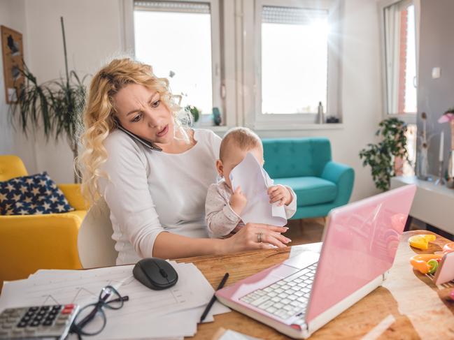 Worried mother holding baby and talking on smart phone at home office