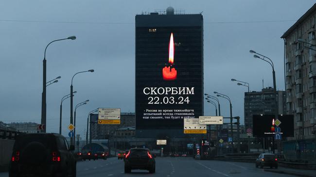 Cars drive past an advertising screen on the facade of a building displaying an image of a lit candle and the words “(We) Mourn 22.03.24” in Moscow. Picture: AFP