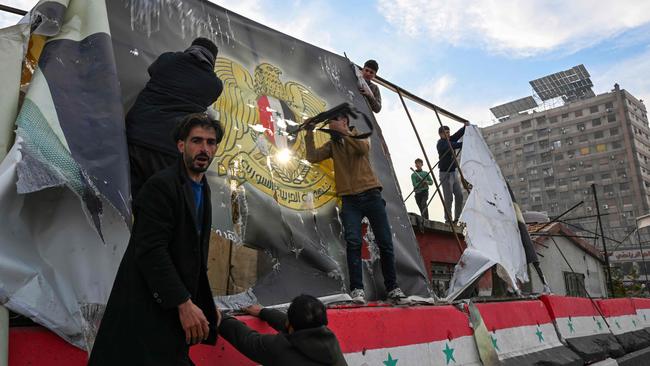 People remove a government banner near Umayyad Square in Damascus on December 8, 2024. Picture: Louai Beshara/AFP