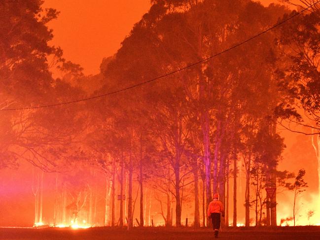 A firefighter walks past burning trees during a battle against bushfires around the town of Nowra in the Australian state of New South Wales on December 31, 2019. - Thousands of holidaymakers and locals were forced to flee to beaches in fire-ravaged southeast Australia on December 31, as blazes ripped through popular tourist areas leaving no escape by land. Picture: Saeed Khan/AFP