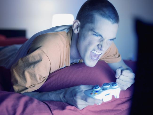 Young adult man playing video game holding Xbox console controller in front of screen.