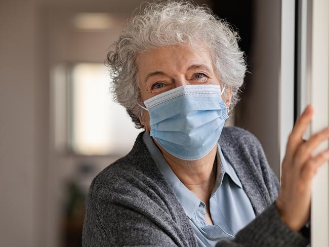 SENIORS -  Portrait of smiling senior woman wearing face mask and standing near window. Old woman with grey hair wearing surgical mask and looking at camera during the lockdown. Happy elderly lady during the covid-19 pandemic stay at home. Picture: Istock