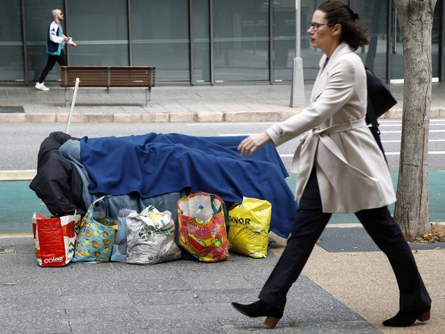 BRISBANE, AUSTRALIA - NewsWire Photos JULY 14, 2023: Pedestrians walk past a homeless man sleeping on a bench in Brisbane. The rental crisis in Queensland are forcing many people on the streets. Picture: NCA NewsWire/Tertius Pickard