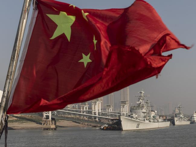 A Chinese national flag flies from a ferry as the retired People's Liberation Army (PLA) Navy Xian frigate ship, from left, and the Huaian frigate ship sit anchored on the Yangtze River in Wuhan, Hubei, China, on Wednesday, Dec. 11, 2019. China's economic growth will come in at 5.9% in 2020 as easing trade tensions and the prospect of lower bank borrowing costs boost confidence, according to analysts and traders. Photographer: Qilai Shen/Bloomberg