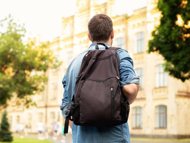 Student university standing with his back to the camera and his backpack on one shoulder and walking in university campus, education concept. Young man walking down street with a backpack. Back view.