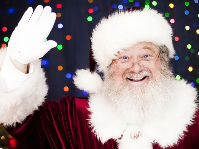 Portrait of a real Santa Claus waving and smiling background with lots of Christmas lights and a decorated Christmas tree. Room for copy space. Merry Christmas!