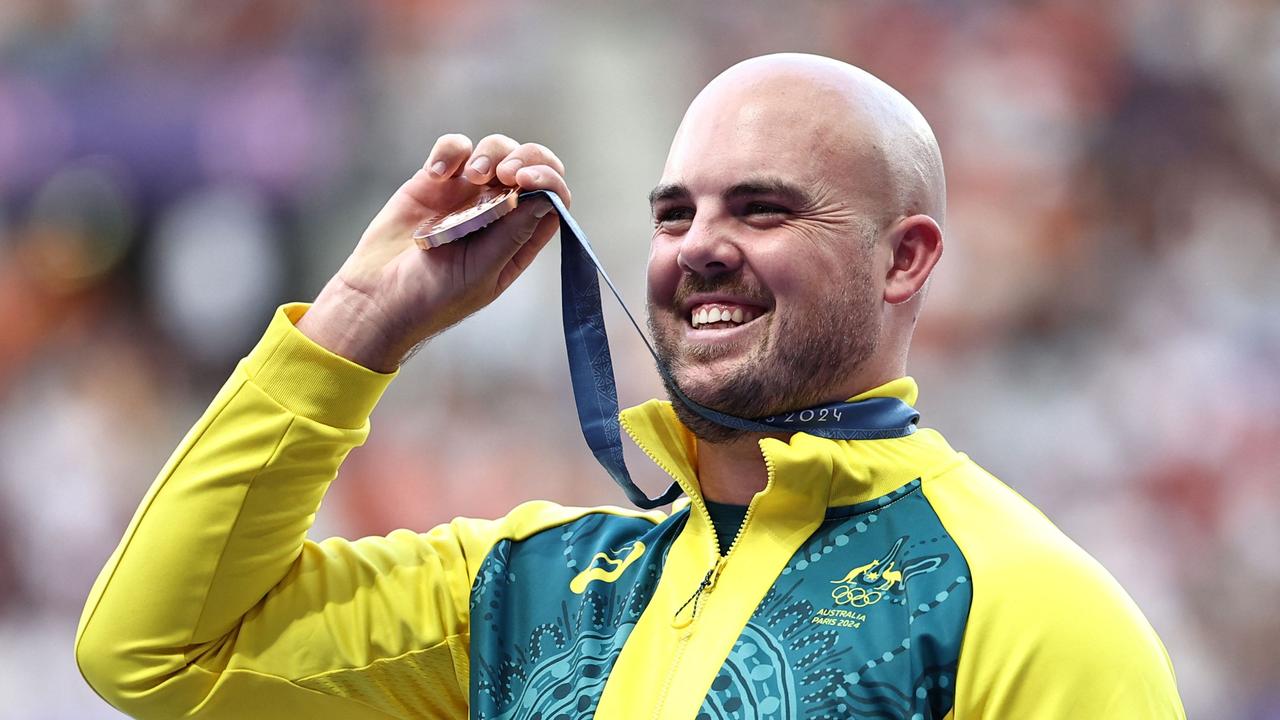 Bronze medallist Australia's Matthew Denny celebrates on the podium during the victory ceremony for the men's discus throw final athletics event at the Paris 2024 Olympic Games at Stade de France in Saint-Denis, north of Paris, on August 8, 2024. (Photo by Anne-Christine POUJOULAT / AFP)