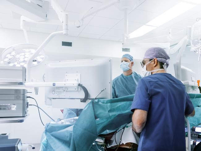 Male surgeons performing laparoscopic surgery. Doctors are monitoring patient in operating room. They are in hospital.