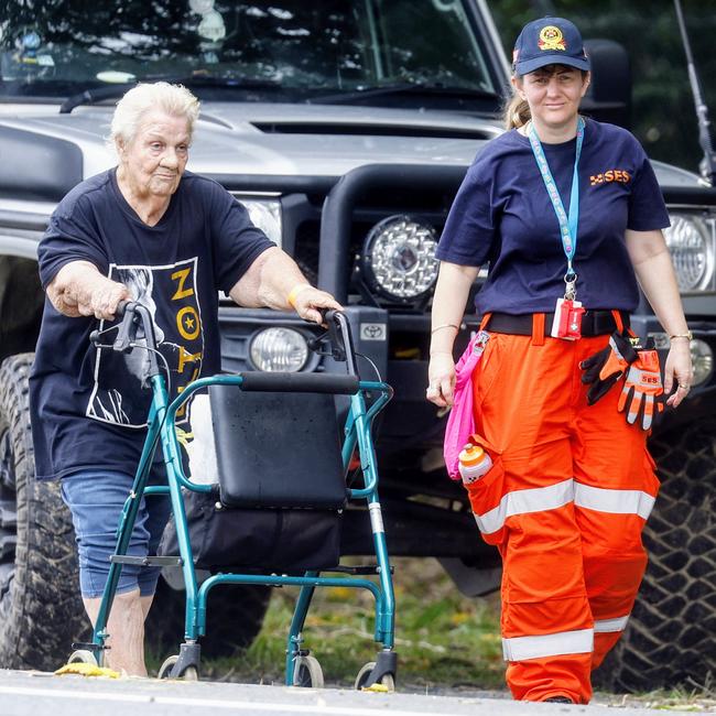 78-year-old Dianna Quick is assisted by a volunteer to be reunited with her granddaughter after spending the night in floodwaters in her Holloways Beach home. Read the full story here . Picture: Brendan Radke
