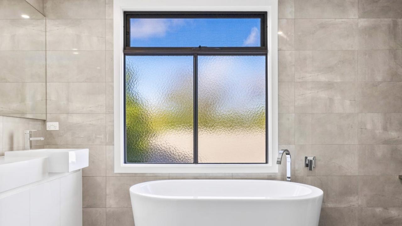 The luxe main bathroom features a freestanding tub, floor-to-ceiling tiling and twin stone vanities.