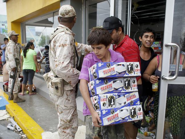 A boy walks away cases of beer from a convenience store destroyed by Hurricane Odile.