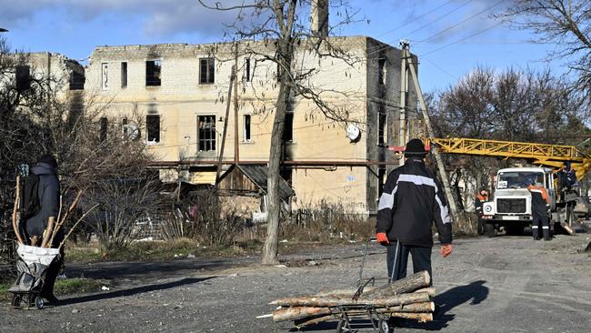 Local residents carry firewood as workers repair power lines in the town of Lyman, Donetsk region, amid the Russian invasion of Ukraine. Picture: AFP