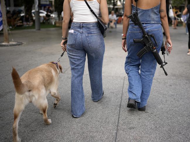 A woman carries an assault rifle as she and a friend walk a dog in downtown Tel Aviv. Picture: Getty Images