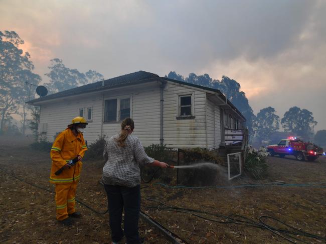A firefighter (L) speaks to a resident trying to hose down her home in the hope of saving it from nearby bushfires around the town of Nowra in the Australian state of New South Wales on December 31, 2019. - Thousands of holidaymakers and locals were forced to flee to beaches in fire-ravaged southeast Australia on December 31, as blazes ripped through popular tourist areas leaving no escape by land. Picture: Saeed Khan/AFP