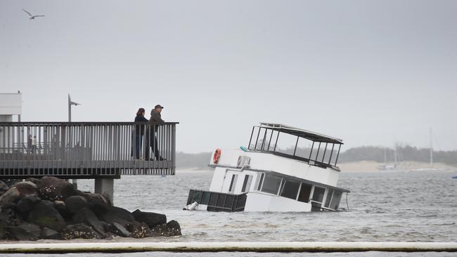 Walkers stop and look at a sunken houseboat washed up by the wild weather on the banks of the Broadwater Parklands at Southport Picture Glenn Hampson.