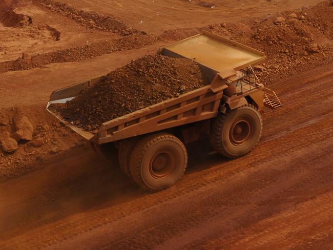 A large haul truck carrying a load of crushed rock and ore on a mine site passing in front of an area being drilled in preparation for blasting; iron ore mining Australia