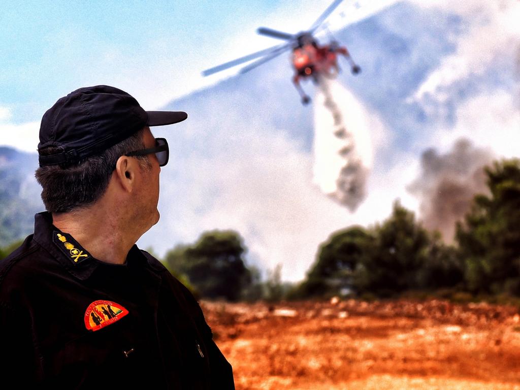 A fireman watches as a helicopter tries to extinguish a wildfire raging in Verori, near Loutraki city, Peloponnese, southern Greece. Picture: EPA/VASSILIS PSOMAS