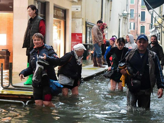 Tourists walk in the flooded streets during a high-water (Acqua Alta) alert in Venice on October 29, 2018. - The flooding, caused by a convergence of high tides and a strong Sirocco wind, reached 156 centimetres on October 29. (Photo by Miguel MEDINA / AFP)