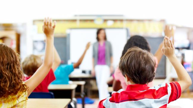 Rear-view of students raising their hands to answer the teacher's question