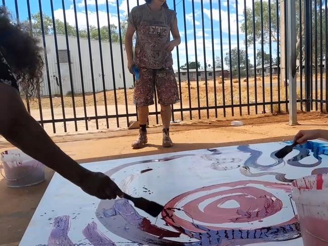 Stills taken from video where a non-indigenous employee is seen contributing to a painting by  (Indigenous) artist  Yaritji Young. The employee wearing darker clothing and holding a paint brush is Rosie Palmer, manager of Tjala Art in the settlement of Amata in the APY Lands.