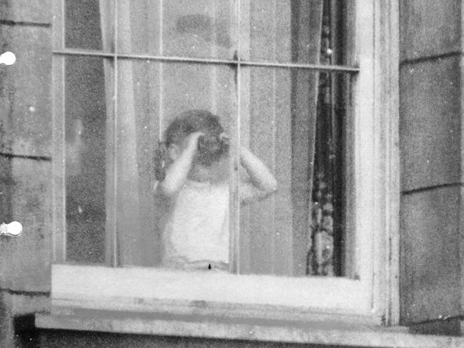 Prince Charles using binoculars to view the Coronation scene from a window at Buckingham Palace.