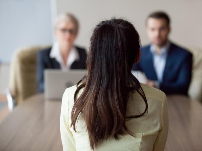 Businesswoman and businessman HR manager interviewing woman. Candidate female sitting her back to camera, focus on her, close up rear view, interviewers on background. Human resources, hiring concept