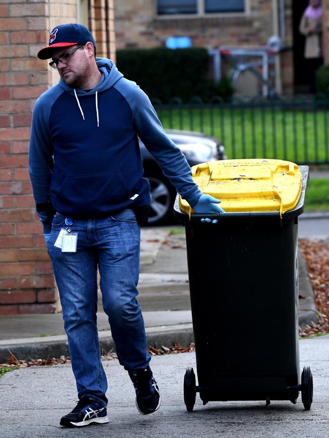 A police officer wearing gloves with a wheelie bin. Picture: Nicole Garmston
