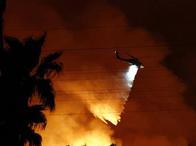 LOS ANGELES, CALIFORNIA - JANUARY 10: A firefighting helicopter drops water as the Palisades Fire burns toward the Mandeville Canyon neighborhood on January 10, 2025 in Los Angeles, California. Multiple wildfires fueled by intense Santa Ana Winds are burning across Los Angeles County. Reportedly at least 10 people have died with over 180,000 people having been under evacuation orders. Over 9,000 structures have been damaged or burned while more than more than 25,000 acres were burning from the fires.   Mario Tama/Getty Images/AFP (Photo by MARIO TAMA / GETTY IMAGES NORTH AMERICA / Getty Images via AFP)