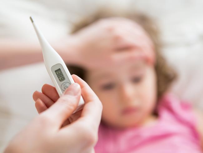 Close-up thermometer. Mother measuring temperature of her ill kid. Sick child with high fever laying in bed and mother holding thermometer. Hand on forehead.