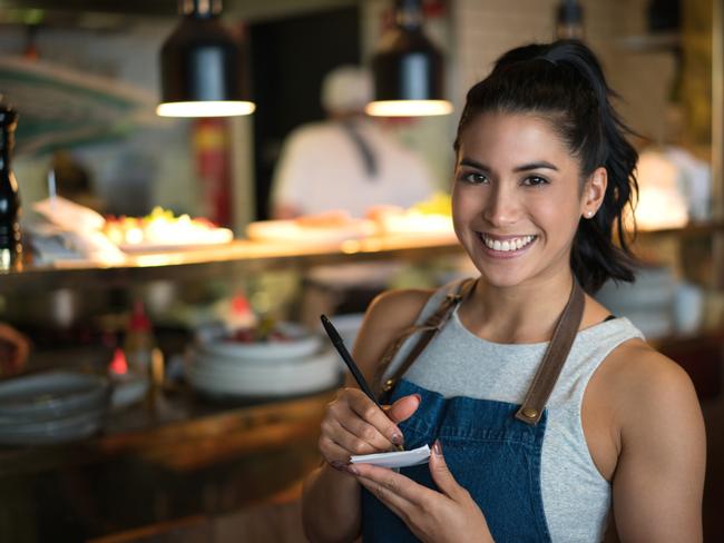 Happy waitress working at a coffee shop and looking at the camera holding a notepad