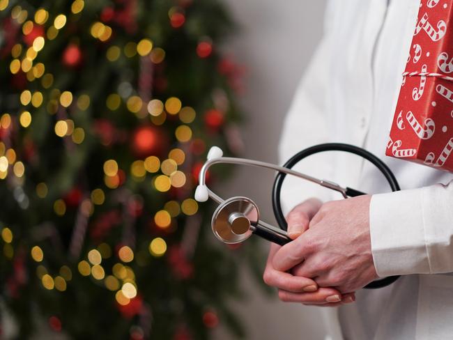 Medical banner concept for Christmas and New Year.Female doctor in white coat holds stethoscope and gift box wrapped in red paper against background of beautifully decorated Christmas tree.Copy space