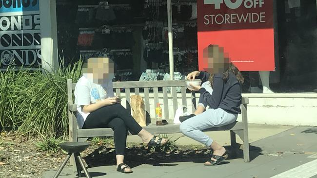 Two young girls eat their food in the sunshine on Hampton St.