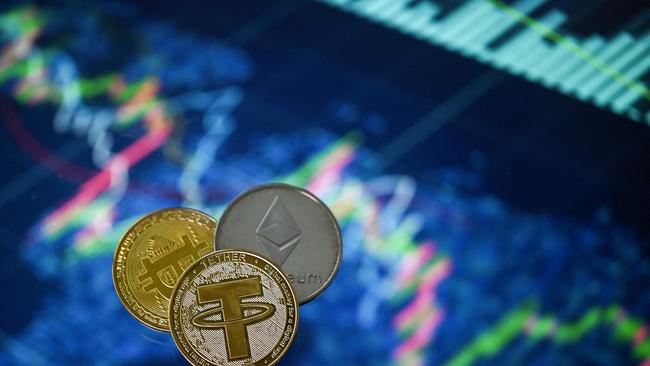 (FILES) This file photo taken in London on May 8, 2022 shows gold plated souvenir cryptocurrency Tether (USDT), Bitcoin and Etherium coins arranged beside a screen displaying a trading chart. (Photo by Justin TALLIS / AFP)