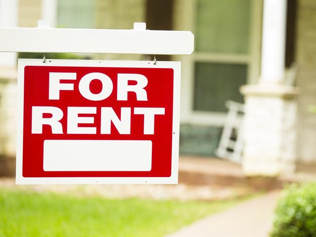 Red and white "House for Rent" sign in front of a stone, wood house that is a rental property. Green grass and bushes indicate the spring or summer season. Front porch and windows in background. Real estate sign in residential neighborhood.  Moving house, relocation concepts.