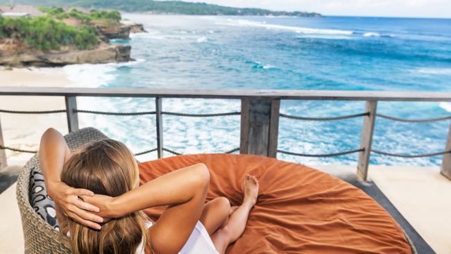 ESCAPE: When holidays go wrong, Paul Ewart - Young woman relaxing in lounge on roof veranda with beautiful tropical sea view. Positive girl look at ocean surf, enjoy vacation. Healthy lifestyle, people on family summer beach holiday. Picture: Istock