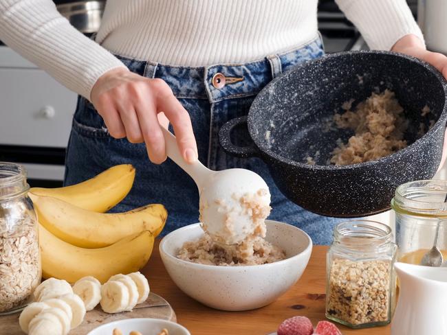 Woman putting oatmeal in a bowl with spoon. Preparing healthy breakfast at the kitchen. Healthy lifestyle concept